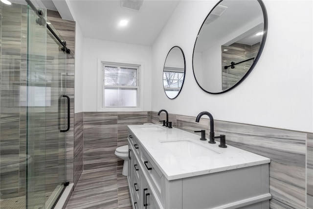 bathroom with vanity, toilet, a shower with door, and tile walls