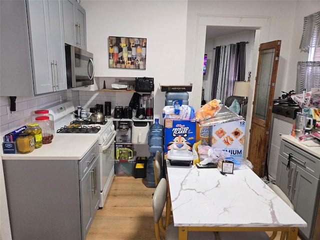 kitchen featuring tasteful backsplash, gray cabinets, light hardwood / wood-style floors, and white gas stove