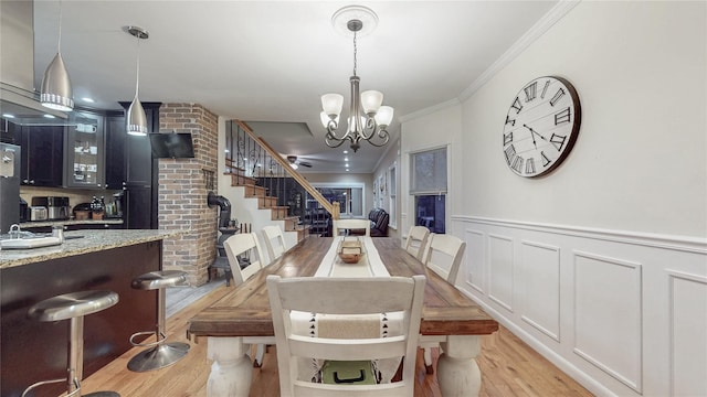 dining space featuring light wood finished floors, a wainscoted wall, stairway, ornamental molding, and a notable chandelier