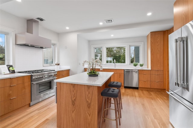 kitchen with a kitchen island, high quality appliances, a kitchen bar, light wood-type flooring, and wall chimney exhaust hood