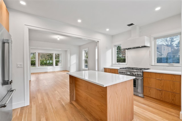 kitchen featuring stainless steel appliances, a center island, wall chimney range hood, and light hardwood / wood-style flooring