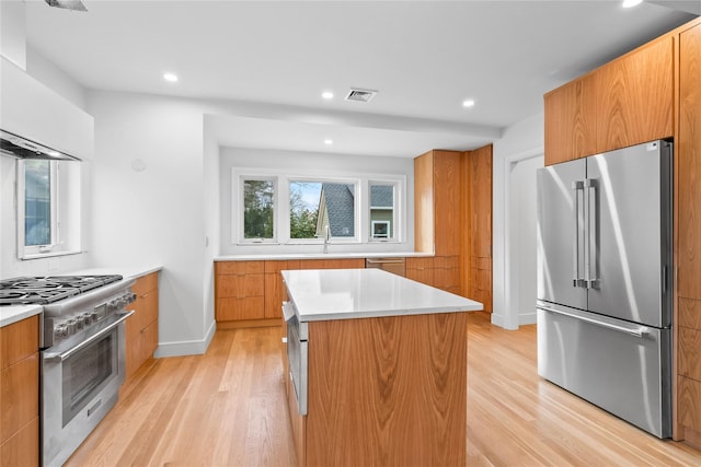 kitchen featuring a kitchen island, high quality appliances, sink, wall chimney exhaust hood, and light hardwood / wood-style flooring