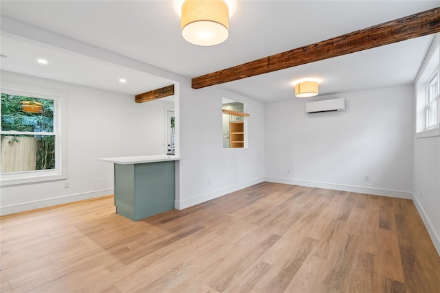 interior space with beamed ceiling, light hardwood / wood-style floors, and an AC wall unit