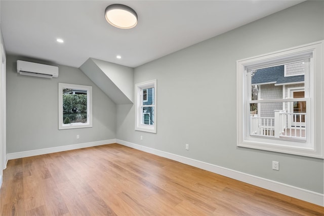 additional living space with a wall mounted AC and light hardwood / wood-style flooring