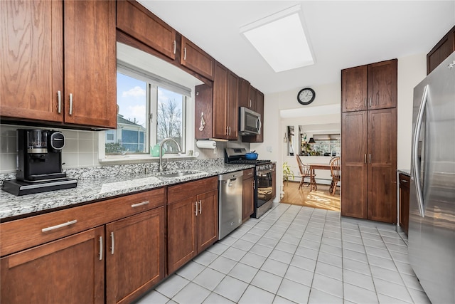 kitchen featuring sink, light tile patterned floors, backsplash, stainless steel appliances, and light stone countertops