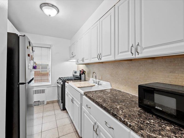 kitchen with light tile patterned flooring, appliances with stainless steel finishes, radiator heating unit, white cabinetry, and sink