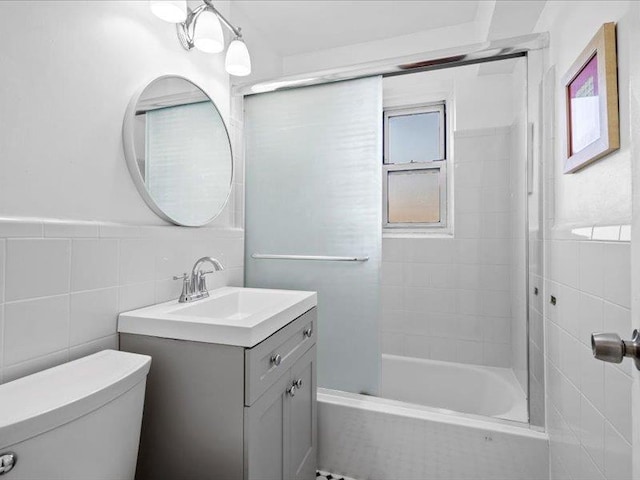 full bathroom featuring tile walls, vanity, tiled shower / bath combo, and toilet