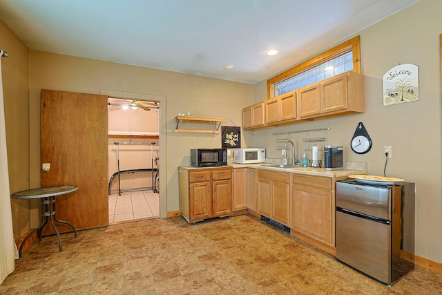 kitchen featuring black microwave, white microwave, light countertops, freestanding refrigerator, and light brown cabinetry