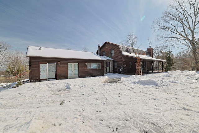 snow covered back of property featuring a chimney, french doors, and a gambrel roof