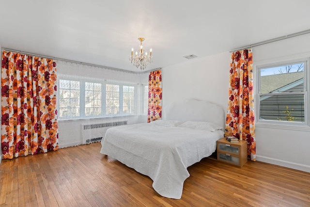 bedroom with radiator heating unit, wood-type flooring, multiple windows, and a notable chandelier