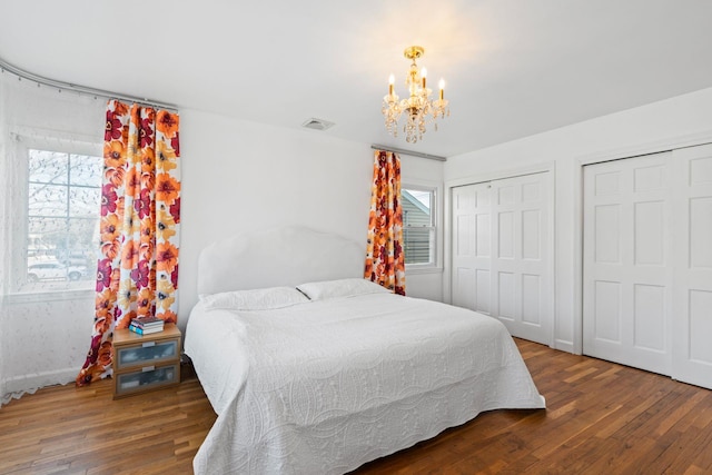 bedroom with dark hardwood / wood-style flooring, two closets, and an inviting chandelier