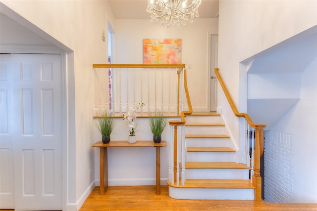 stairway with a chandelier, wood finished floors, and baseboards