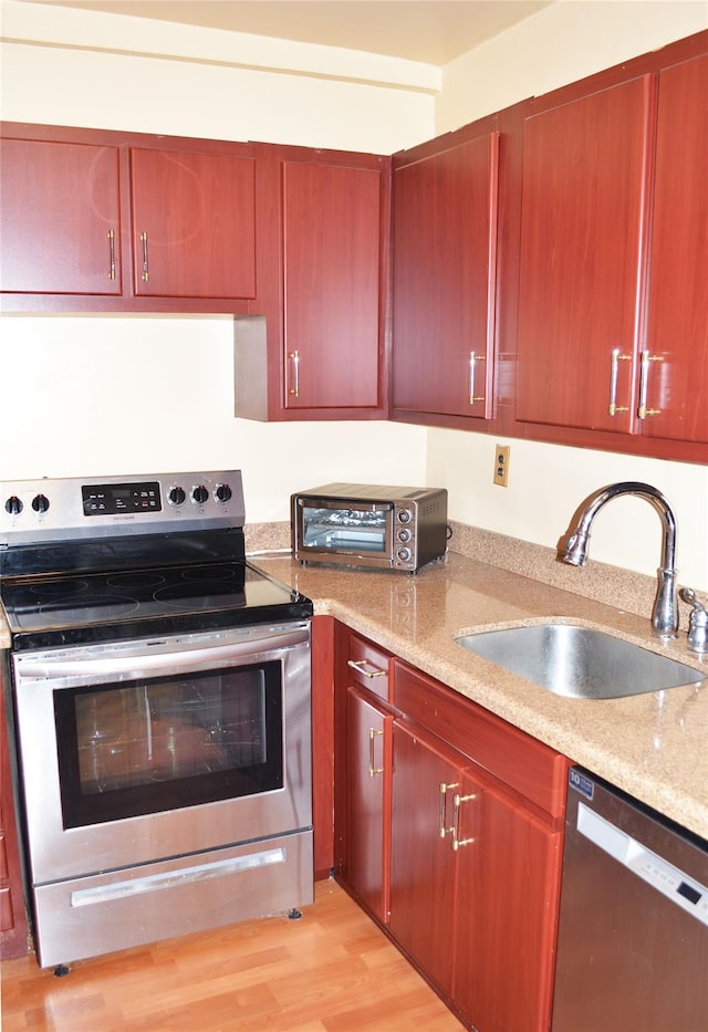 kitchen featuring light stone countertops, appliances with stainless steel finishes, sink, and light hardwood / wood-style flooring