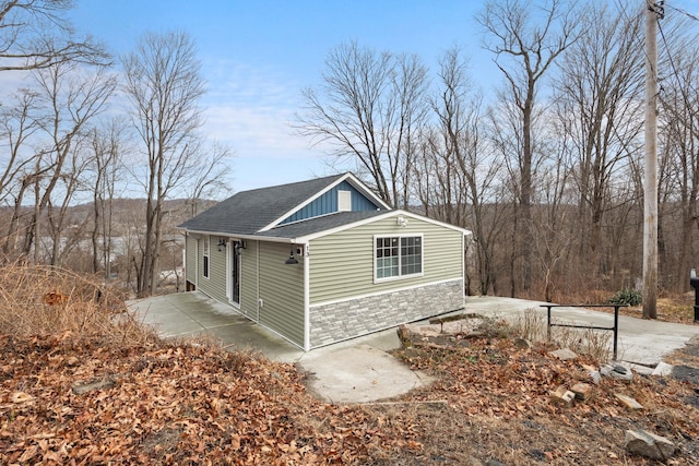 exterior space featuring a shingled roof and stone siding