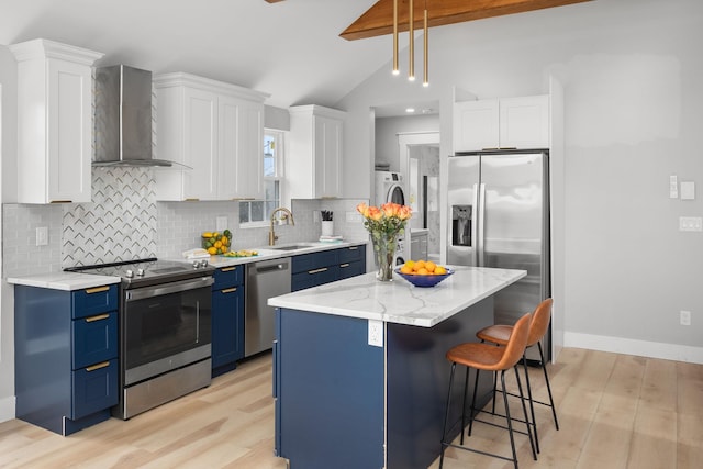 kitchen with a sink, stainless steel appliances, separate washer and dryer, blue cabinetry, and wall chimney range hood