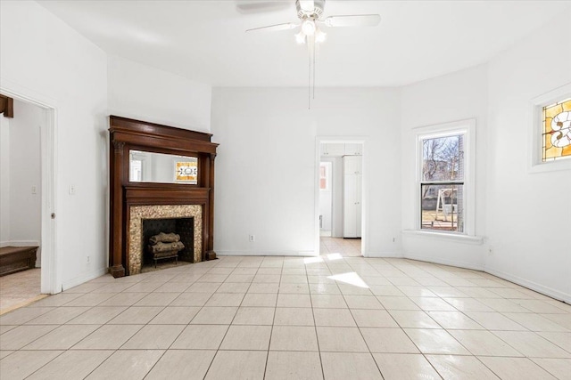 unfurnished living room with light tile patterned floors, ceiling fan, baseboards, and a tile fireplace