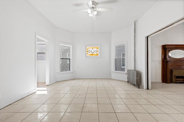 empty room with radiator, light tile patterned floors, ceiling fan, and baseboards