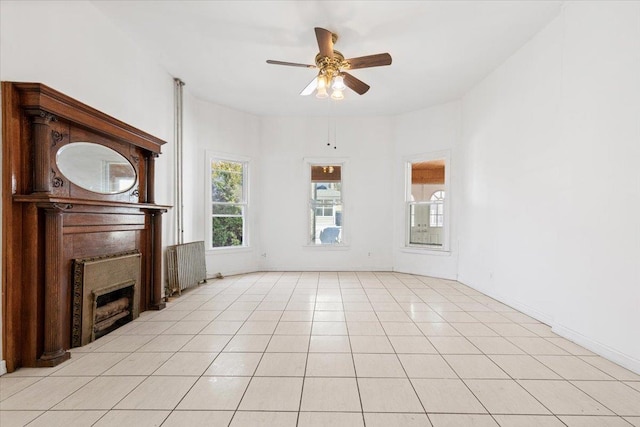 unfurnished living room with a ceiling fan, radiator, a fireplace, and light tile patterned floors