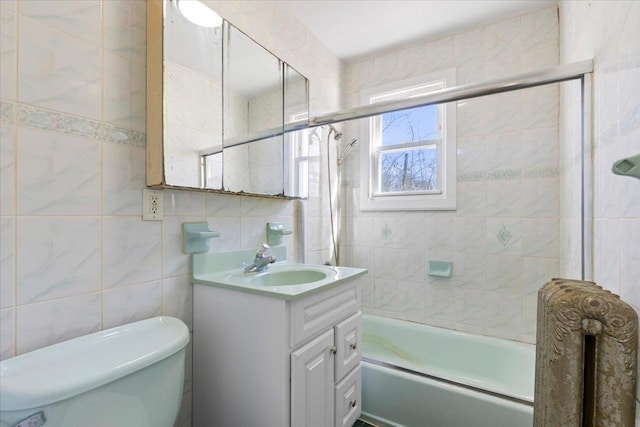 bathroom with toilet, combined bath / shower with glass door, vanity, and tile walls