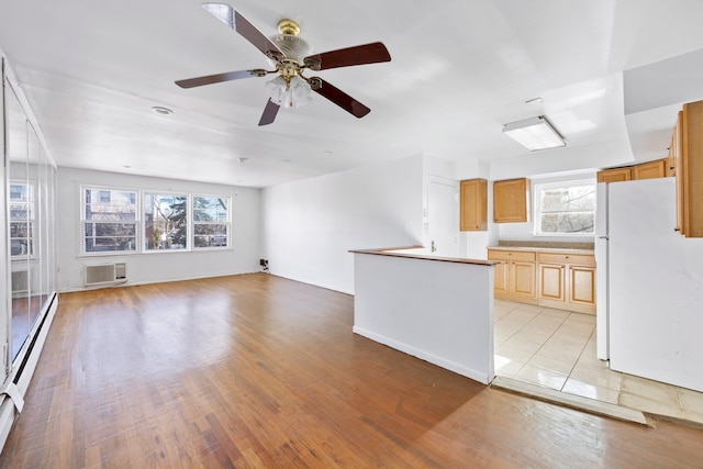 unfurnished living room featuring ceiling fan, a baseboard heating unit, a wall mounted AC, and light hardwood / wood-style floors