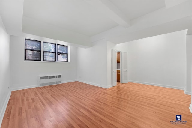 empty room featuring beamed ceiling, radiator heating unit, and light hardwood / wood-style flooring