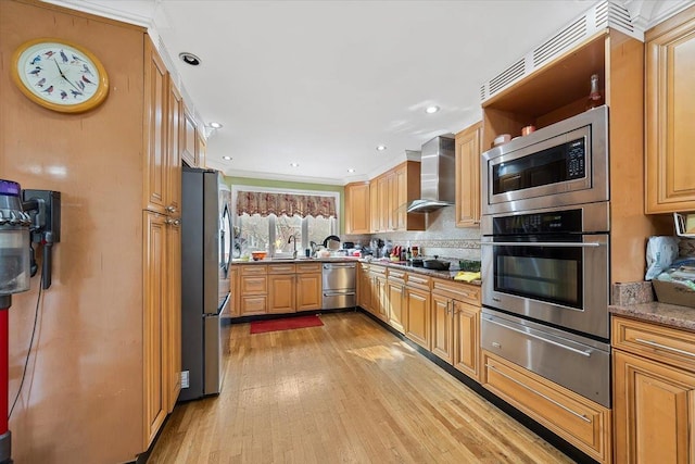 kitchen with appliances with stainless steel finishes, backsplash, wall chimney exhaust hood, light stone counters, and light hardwood / wood-style flooring