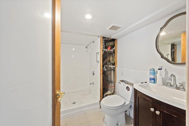 bathroom with tiled shower, vanity, toilet, and tile walls