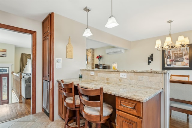 kitchen featuring a breakfast bar, light stone counters, a wall mounted air conditioner, decorative light fixtures, and kitchen peninsula