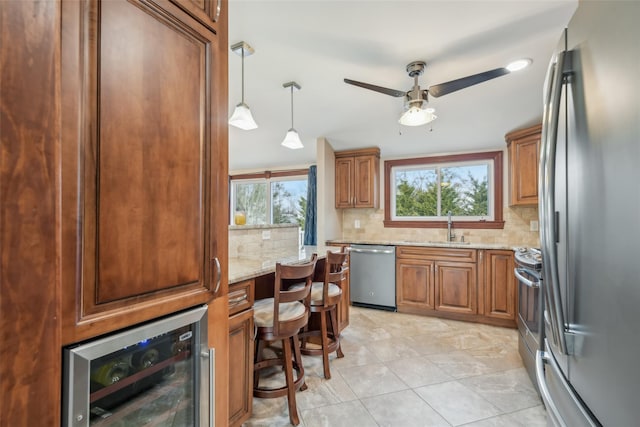 kitchen with wine cooler, sink, hanging light fixtures, stainless steel appliances, and light stone countertops