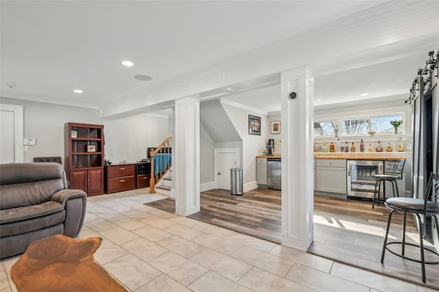 living room with crown molding, bar area, wine cooler, and light hardwood / wood-style flooring