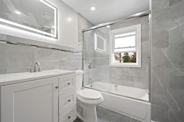 full bathroom featuring vanity, tile walls, shower / bath combination with glass door, and toilet