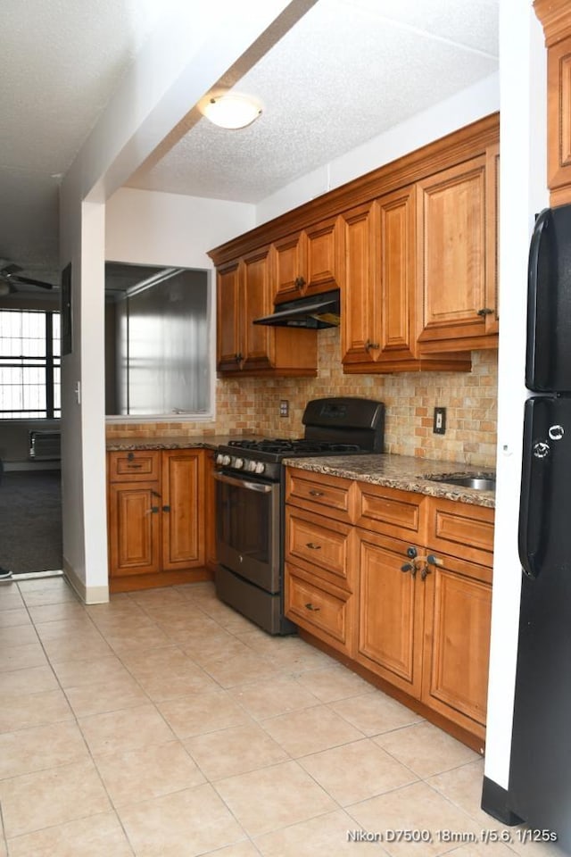 kitchen with tasteful backsplash, black fridge, light stone counters, and gas range oven