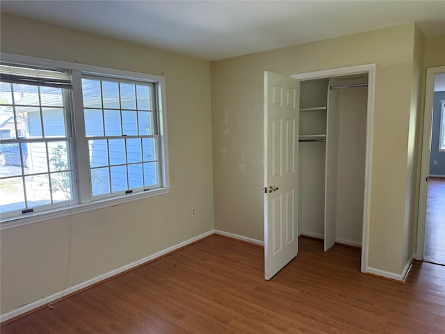 unfurnished bedroom with multiple windows, light wood-style floors, baseboards, and a closet