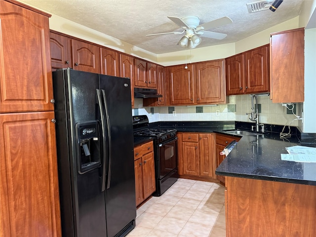 kitchen with black appliances, a sink, under cabinet range hood, ceiling fan, and dark stone countertops