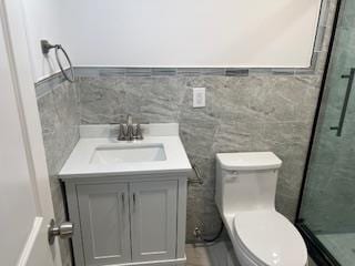 bathroom featuring vanity, toilet, tile walls, and a shower with shower door