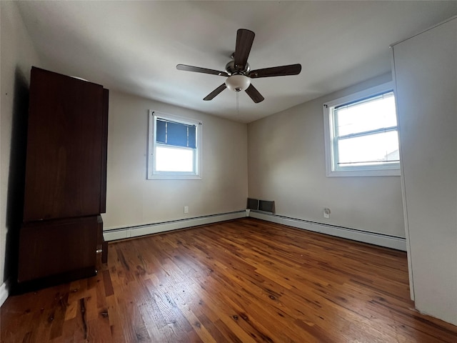 empty room featuring dark hardwood / wood-style flooring, a baseboard heating unit, and a healthy amount of sunlight