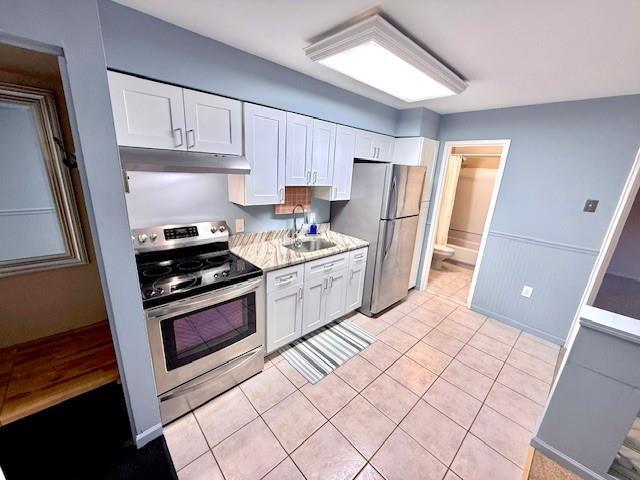 kitchen with light tile patterned flooring, appliances with stainless steel finishes, white cabinetry, sink, and light stone counters