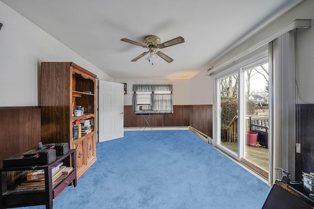 interior space with baseboard heating, ceiling fan, carpet floors, and wood walls