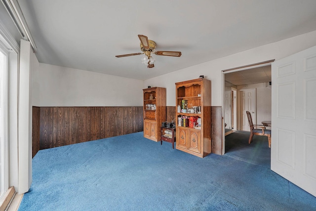 unfurnished room featuring wood walls, ceiling fan, and dark colored carpet