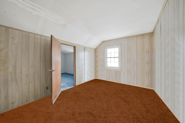 additional living space featuring lofted ceiling, light carpet, and wood walls