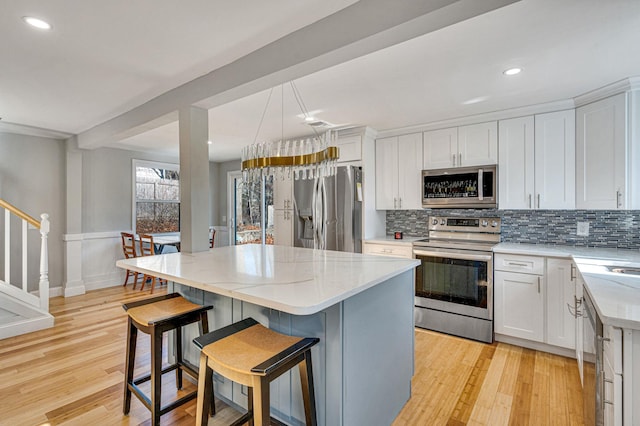 kitchen featuring white cabinetry, a kitchen breakfast bar, stainless steel appliances, a center island, and tasteful backsplash