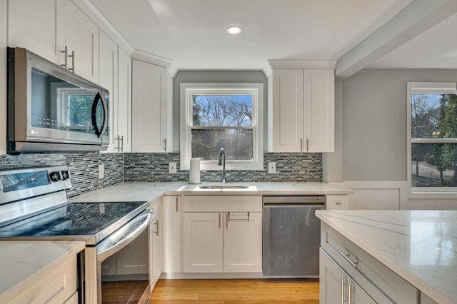 kitchen with sink, stainless steel appliances, light stone countertops, light hardwood / wood-style floors, and white cabinets