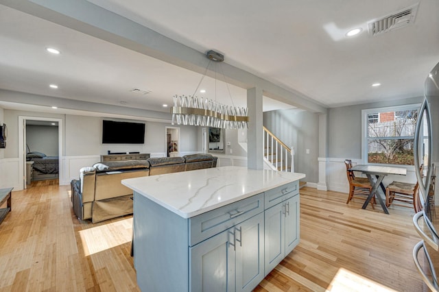 kitchen with light stone countertops, a center island, stainless steel fridge, and light hardwood / wood-style floors