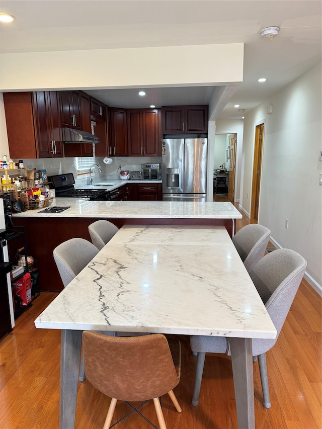 kitchen with appliances with stainless steel finishes, sink, a breakfast bar area, kitchen peninsula, and light hardwood / wood-style flooring