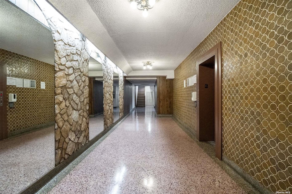 corridor with decorative columns, elevator, and a textured ceiling