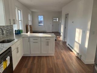 kitchen with sink, a baseboard radiator, kitchen peninsula, dishwasher, and white cabinets