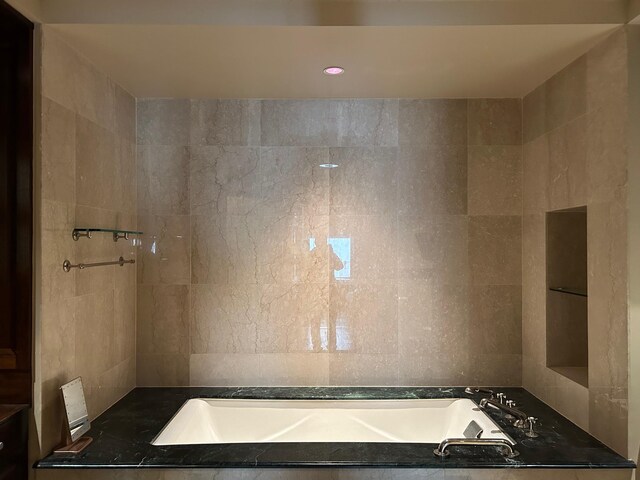 bathroom featuring a relaxing tiled tub and tile walls