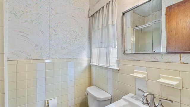 bathroom with toilet, sink, tile walls, and a shower with shower door