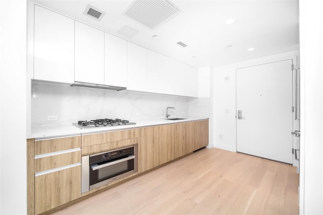 kitchen featuring tasteful backsplash, stainless steel appliances, light hardwood / wood-style floors, and white cabinets