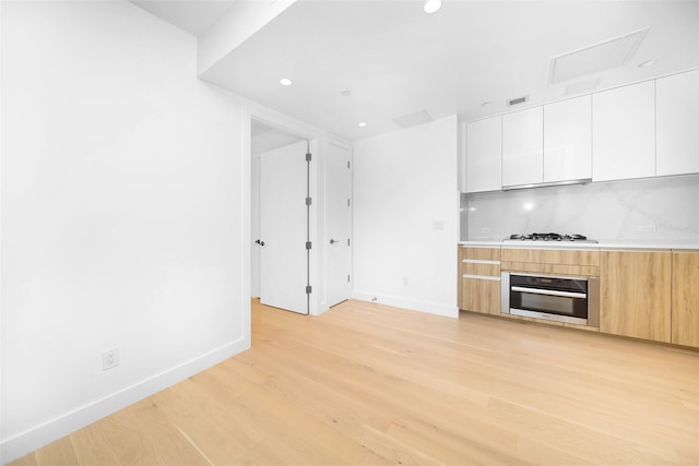 kitchen with white cabinetry, light wood-type flooring, oven, and backsplash